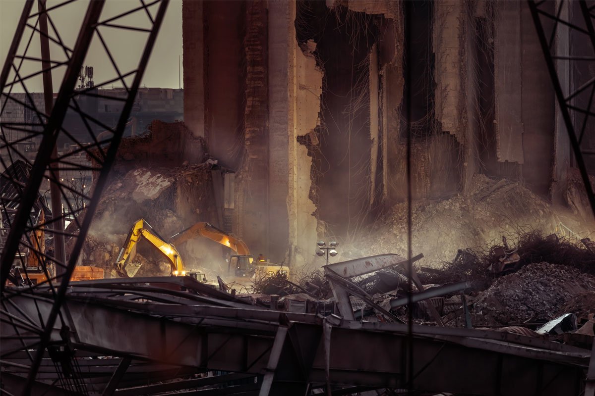 Two excavators demolishing a large building, creating a cloud of dust and debris. | Forensic Discovery