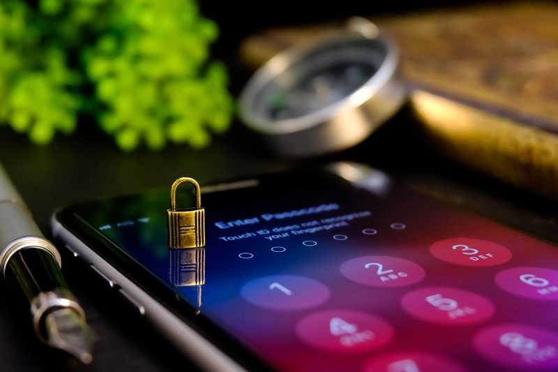 A small gold padlock sits on a smartphone screen displaying a passcode entry screen.