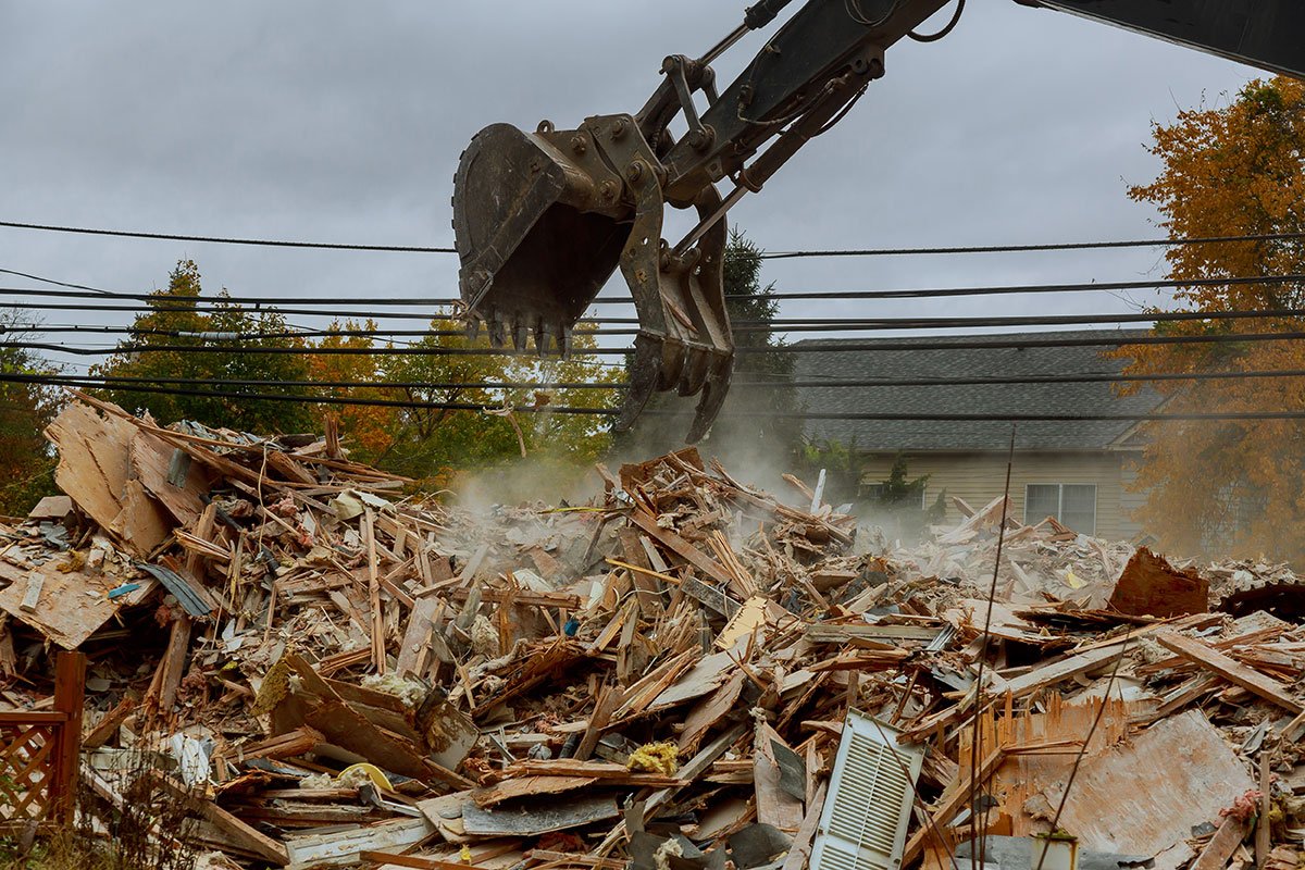 Excavator bucket demolishing a building and piling debris. | Forensic Discovery