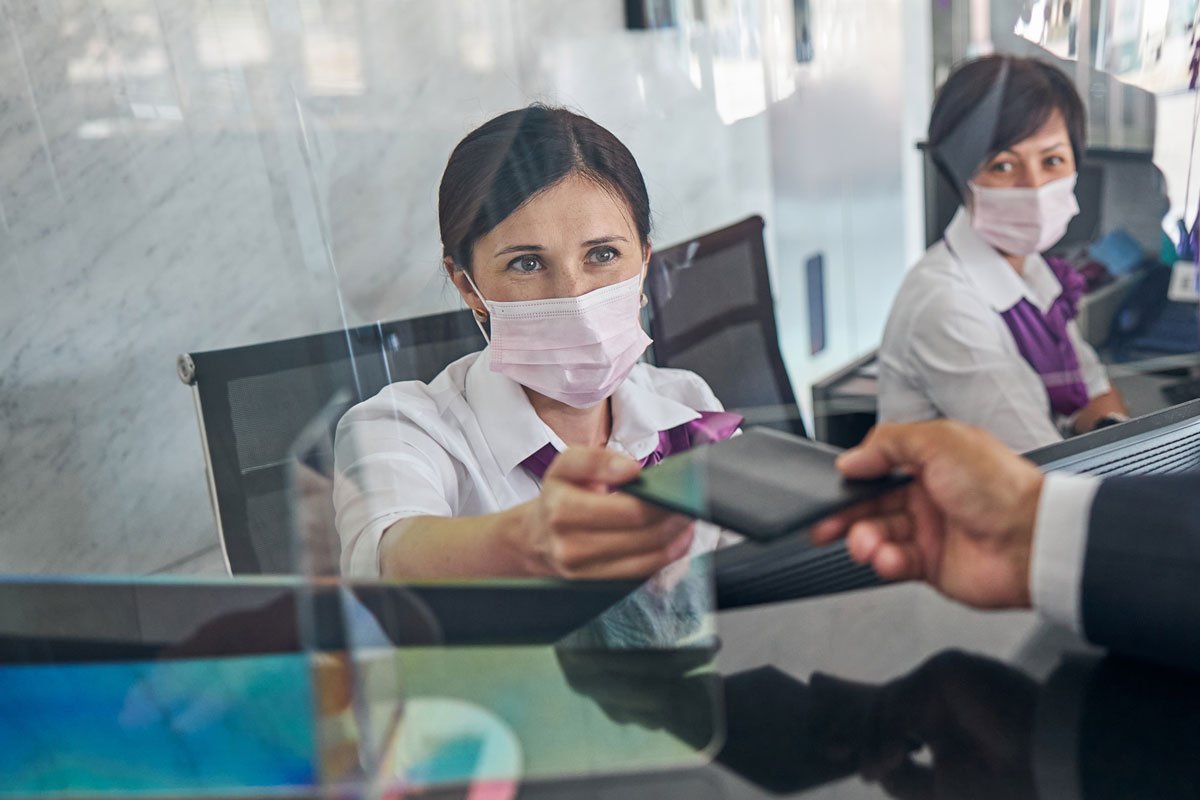 Woman in a mask handing a phone or card across a protective barrier to a person in a suit. | Forensic Discovery
