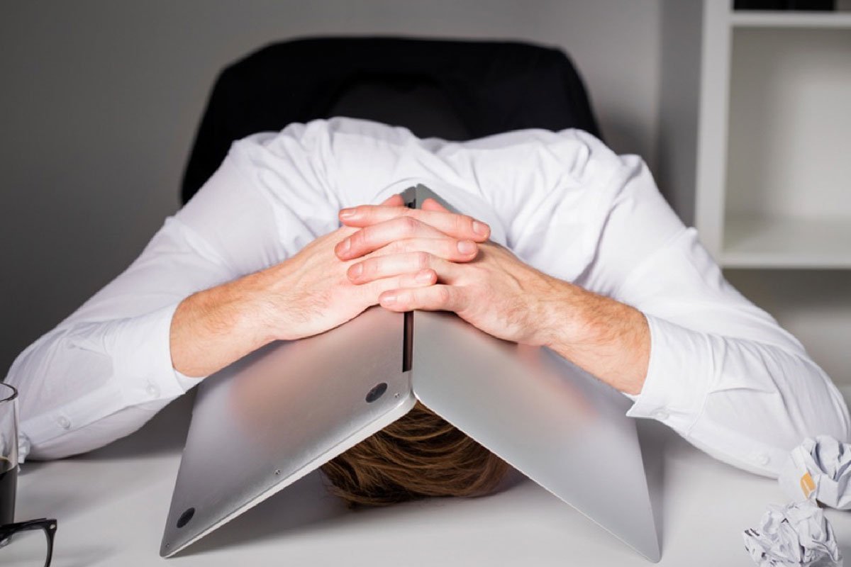 Person in a white shirt with their head resting on a laptop, hands clasped on top. | Forensic Discovery