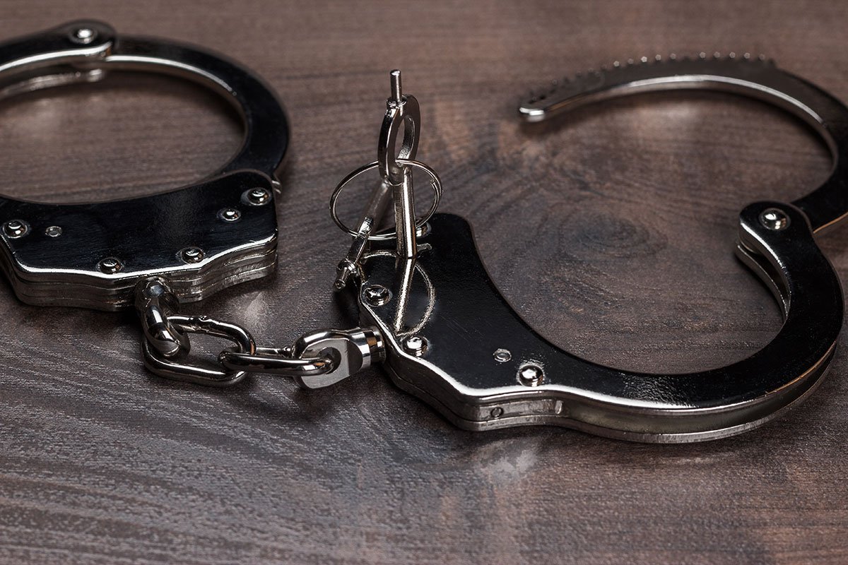 Pair of handcuffs and key on a dark wooden surface. | Forensic Discovery