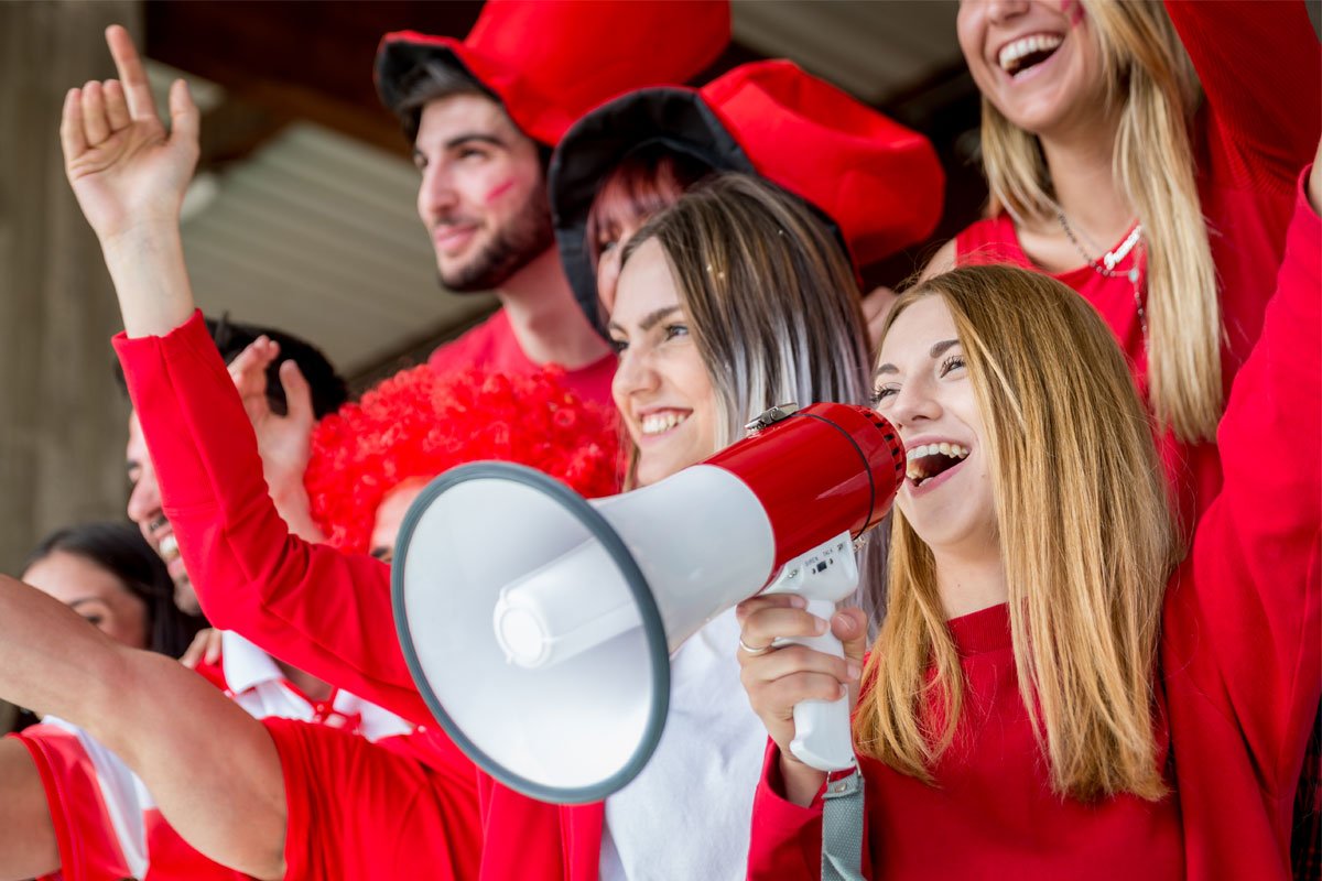 A group of excited sports fans in red clothing, one of whom is using a megaphone. | Forensic Discovery