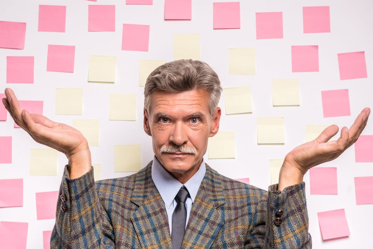 A man in a tweed jacket stands with his arms out to his sides, looking overwhelmed by a wall covered in sticky notes. | Forensic Discovery